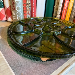 Könnte beinhalten: Ein grünes Glasserviertablett mit sechs unterteilten Abschnitten. Das Tablett hat ein Blumenmuster und einen perlenbesetzten Rand. Das Tablett liegt auf einer Schachtel mit dem aufgedruckten Text "INDIANA GLASS".