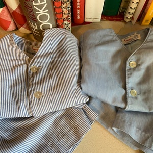 May include: Two button-up shirts, one with blue and white stripes and the other a solid light blue. Both shirts have a v-neck and are made of a soft, textured fabric.