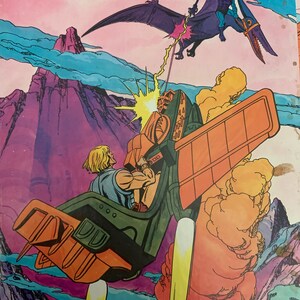 May include: A 200 piece Golden puzzle featuring He-Man flying in his battle-pod, firing a laser beam at a purple flying creature with a sword. The background is a purple and blue sky with a mountain in the distance.
