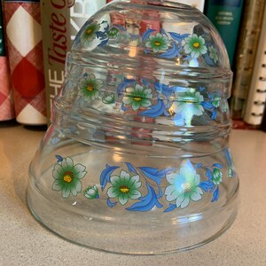 May include: A set of three clear glass mixing bowls with a blue and green floral design. The bowls are stacked on top of each other.