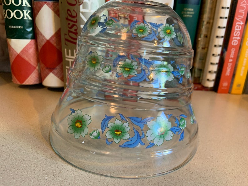 May include: A set of three clear glass mixing bowls with a blue and green floral design. The bowls are stacked on top of each other.