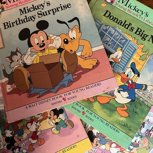 May include: A stack of five colourful children's books featuring Mickey Mouse and Donald Duck characters. The books are titled "Mickey's Birthday Surprise", "Mickey's Donald's Big News", and "Disney's Guide to", with the last two titles partially obscured. The books are all part of the "A Walt Disney Book for Young Readers" series.