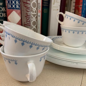 May include: White ceramic teacups and saucers with a blue floral design. The cups are stacked, and the saucers are in a neat pile. The set is part of a vintage dinnerware collection, perfect for serving tea or coffee.