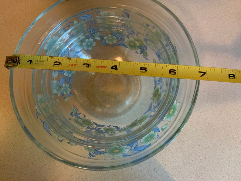 May include: Set of four glass mixing bowls with a floral design in shades of blue and green. The bowls are nested inside each other and measure 8 inches in diameter.