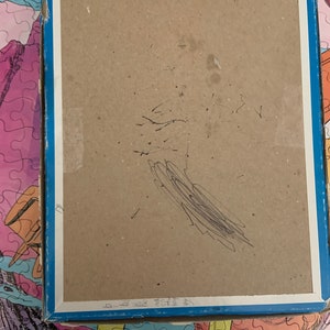 May include: The back of a cardboard box for a jigsaw puzzle. The box is brown and has a blue border. There are some black scribbles on the back of the box.