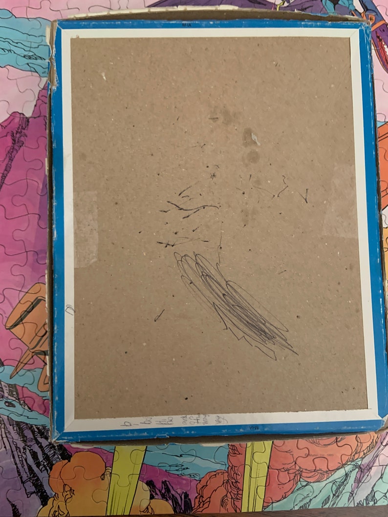 May include: The back of a cardboard box for a jigsaw puzzle. The box is brown and has a blue border. There are some black scribbles on the back of the box.