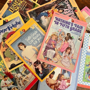 Puede incluir: Una pila de libros de bolsillo coloridos con títulos como "Stage Fright", "Nada es justo en quinto grado" y "Alquilar un trabajo en tercer grado". Los libros son todos parte de la serie "Apple Paperbacks" y presentan ilustraciones de niños en las portadas.