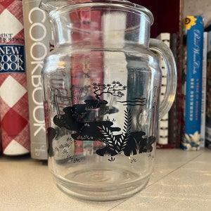 Könnte beinhalten: Eine klare Glaskanne mit einem schwarz-weißen Design eines japanischen Gartens. Das Design beinhaltet einen Teich, Bäume und Pflanzen.