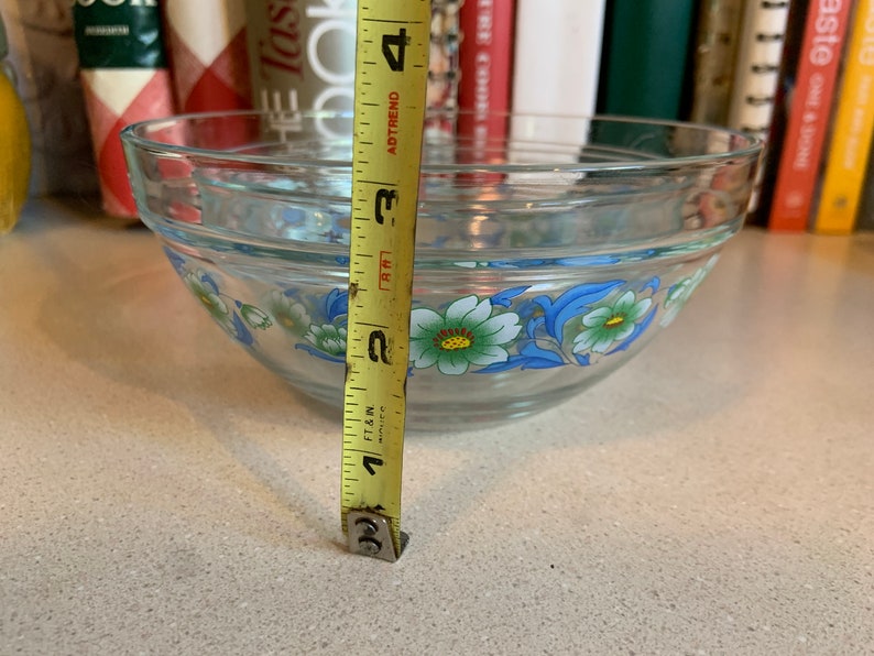 May include: A clear glass mixing bowl with a floral design in blue, white, and green. The bowl is 3 inches tall.