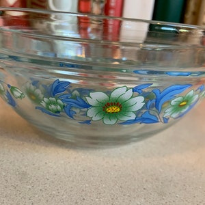 May include: A clear glass mixing bowl with a floral design. The bowl has a blue, green, and white floral pattern.