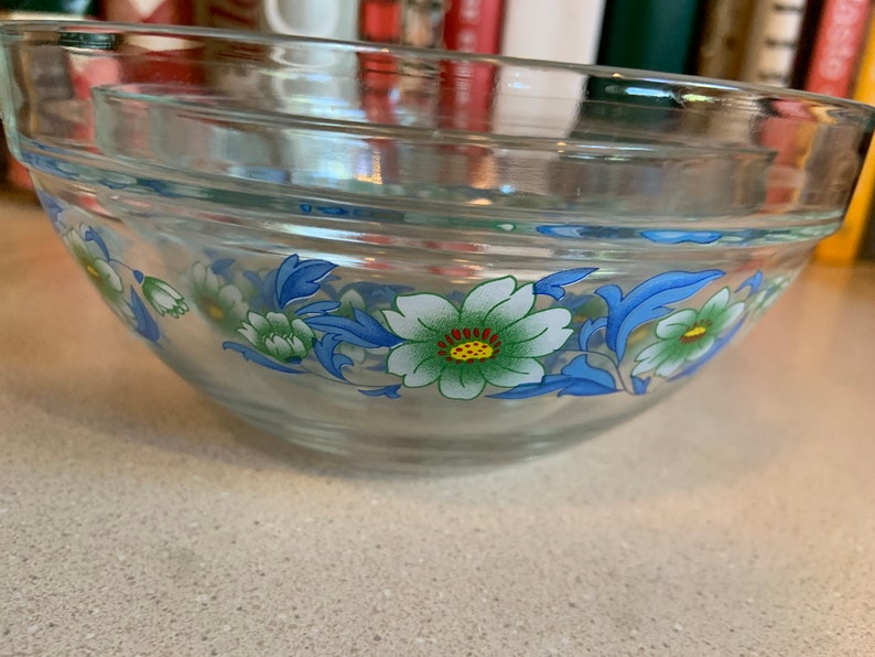 May include: A clear glass mixing bowl with a floral design. The bowl has a blue, green, and white floral pattern.