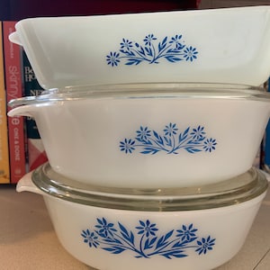 May include: Three white ceramic baking dishes with blue floral designs. The dishes are stacked on top of each other. The top dish is a rectangular baking dish, the middle dish is a round baking dish, and the bottom dish is a round baking dish with a lid.