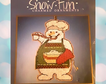 May include: A Snow Fun Charmed Ornaments counted glass bead kit titled MH16-2135 Cooking Snowman. The package displays a cross-stitch snowman wearing a chef hat, a green apron, and a red oven mitt, holding a spoon and a metal key charm. Size: 2.5"w x 3.5"h.