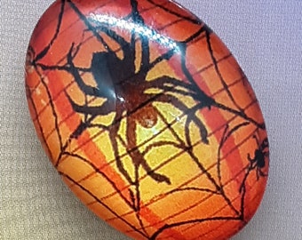 May include: A round, orange and black glass cabochon with a spider web design and a black spider in the center.