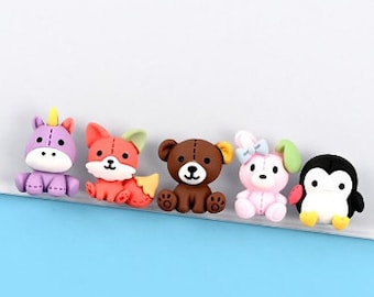 May include: Five colorful, small, cartoon animal figurines. A purple unicorn, an orange fox, a brown bear, a pink bunny rabbit, and a black penguin.