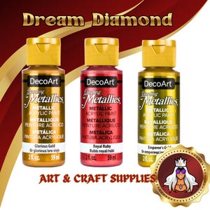 May include: Three bottles of DecoArt Dazzling Metallics acrylic paint in gold, red, and green. Each bottle has a gold cap and label with the paint name and volume (59 ml). The text "Dream Diamond" and "Art & Craft Supplies" are also visible.
