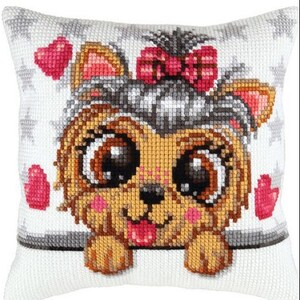 May include: A white pillow with a cross-stitch design of a brown and tan Yorkshire Terrier puppy with big brown eyes. The puppy is wearing a pink bow and is surrounded by pink hearts.