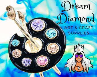 May include: A black paint palette with a gold paintbrush and rhinestones. The palette has seven sections, each with a different colored rhinestone. The image includes the text "Dream Diamond Art & Craft Supplies".