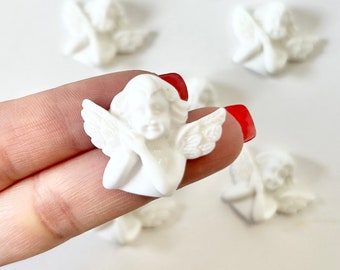 May include: A set of eight small white ceramic angel figurines. The angels are in a variety of poses, with some holding flowers and others with their wings spread.