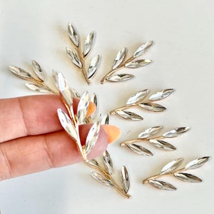 May include: A set of seven gold leaf embellishments with clear rhinestone accents. Each leaf is approximately 1.5 inches long.