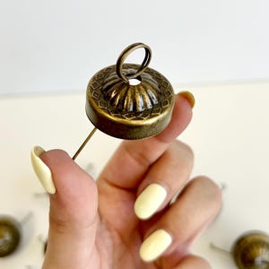 May include: A collection of antique brass clock pendulum bobs. The bobs have a decorative, ridged design and a small loop at the top. The bobs are attached to a thin metal rod.