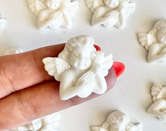May include: A collection of small, white cherub figurines. Each cherub has detailed wings and is holding a musical instrument. The figurines are arranged on a white surface.