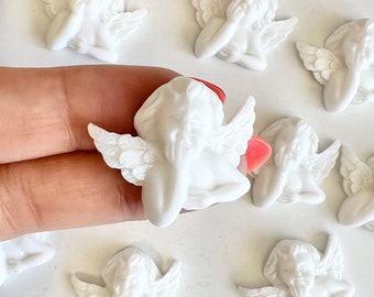 May include: A collection of small, white cherub figurines with detailed wings and serene expressions. Some cherubs have a touch of red and pink. These decorative figurines are ideal for crafts or embellishments.