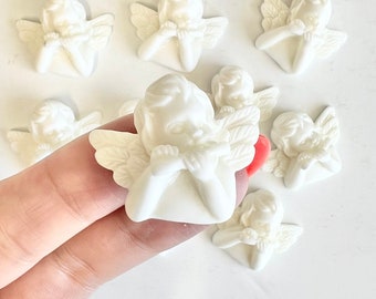 May include: A group of eight white ceramic angel figurines with wings, each with their hands clasped in front of their faces. The angels are all facing forward and have a simple, elegant design.