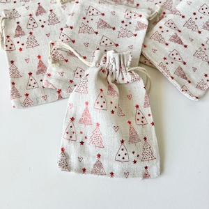 Könnte beinhalten: Ein Set kleiner, weißer Stoffgeschenktüten mit einem roten Weihnachtsbaum-Muster. Die Taschen haben einen Kordelverschluss und sind perfekt für kleine Geschenke oder Mitbringsel.