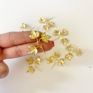 May include: A group of gold-colored metal leaf sprigs. Each sprig has three leaves and a stem. The leaves are detailed and have a textured surface.