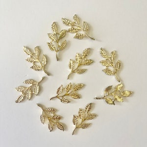 May include: A set of ten gold-colored metal leaf sprigs. Each sprig has a delicate, intricate design with multiple leaves.