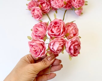 May include: A bunch of pink silk rose flower buds with green stems. The flowers are arranged in a bouquet and are held in a hand.