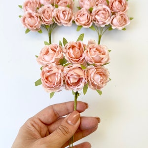 May include: Two bunches of pale pink silk rose flower buds with green stems and leaves.