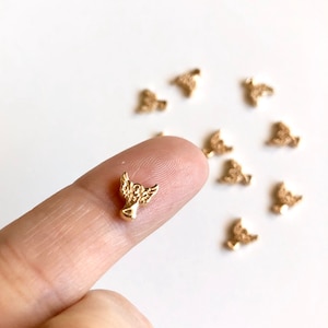 May include: A close-up of a gold angel charm with wings. The charm is small and delicate, and it is perfect for adding a touch of whimsy to jewelry or crafts.