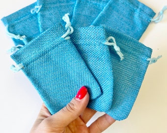 Op de afbeelding: Een set van zes kleine, lichtblauwe trekkoordzakjes gemaakt van een textuurstof. De zakjes zijn perfect voor kleine cadeautjes of attenties.
