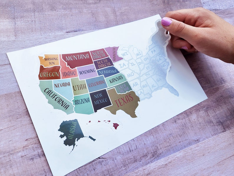 May include: A colorful map of the United States with each state labeled. The map is printed on white paper and has a light blue outline. The map is being peeled off of a sheet of paper.