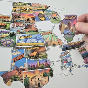 Op de afbeelding: Een kaart van de Verenigde Staten met kleurrijke staatsillustraties. De kaart toont staatsnamen en iconische afbeeldingen, waaronder bezienswaardigheden en dieren in het wild. Een Illinois-sticker wordt omhoog gehouden, klaar om op de kaart te worden geplakt.