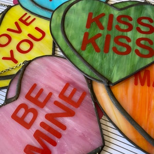 May include: Assortment of stained glass heart ornaments with various Valentine's Day messages, including "Love You", "Kiss Kiss", "Be Mine", and "Marry Me".