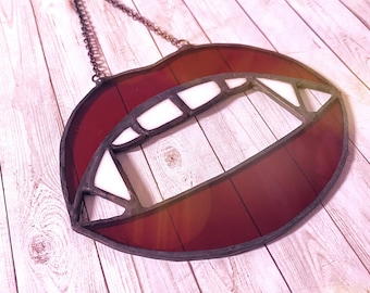 Puede incluir: Una ventana de vitral colgante con un diseño rojo, blanco y negro de una boca con colmillos.