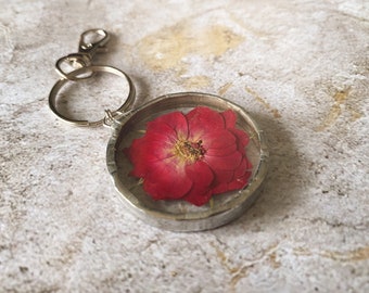 May include: A silver key chain with a round resin charm featuring a pressed red flower.
