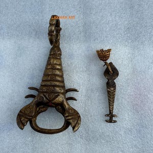 May include: Two antique bronze bottle openers. One is scorpion-shaped with a handle, the other is a small key-shaped opener with a crown. The text "LAXMAN ART" is visible on the scorpion opener.