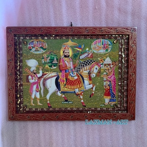 May include: A framed religious artwork depicting a man riding a white horse. The artwork is set against a green background with gold accents. The man is wearing a red and gold robe and a crown. The horse is adorned with gold and silver embellishments. The artwork is surrounded by a brown wooden frame with gold accents.