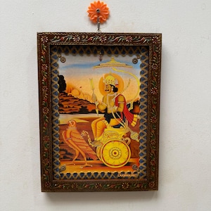 以下が含まれることがあります： 弓と矢を持った人物が描かれた、宗教的な額入りのプリント。鳥と金の車輪が描かれています。茶色のフレームには装飾的なディテールがあります。プリントは白い壁に掛けられています。