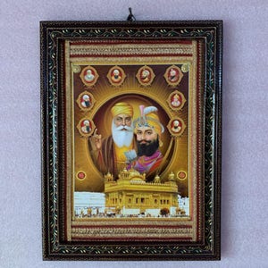 May include: A framed image of two Sikh gurus, Guru Nanak and Guru Gobind Singh, with a golden temple in the background. The image is surrounded by a decorative frame with gold and red accents.
