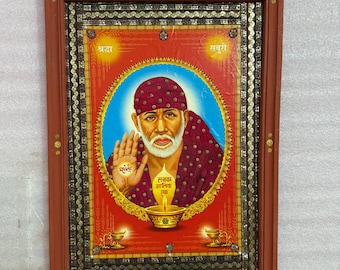 May include: A framed religious artwork featuring a central portrait of a spiritual figure with a white beard and a maroon turban. The image is set against a red background with gold accents and text. The frame is a dark reddish-brown color.