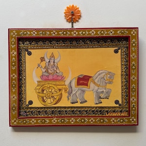 May include: A framed painting depicting a deity in a chariot pulled by a white horse. The artwork features a yellow background, intricate gold detailing, and the text "LAXMAN ART" in the lower right corner. The frame is red with gold accents.