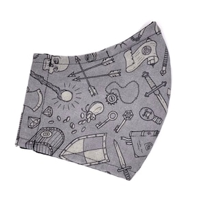 May include: A gray fabric face mask with a black and white print of various fantasy and adventure themed icons, including a skull, arrows, a sword, a shield, a key, a treasure chest, and a magic wand.