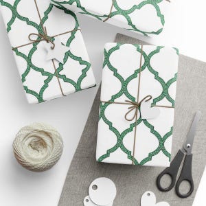 May include: Several wrapped gifts with white paper and a green geometric pattern are tied with twine and adorned with white paper cutouts. A ball of twine, scissors, and additional cutouts are also visible.