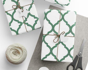 May include: Several wrapped gifts with white paper and a green geometric pattern are tied with twine and adorned with white paper cutouts. A ball of twine, scissors, and additional cutouts are also visible.