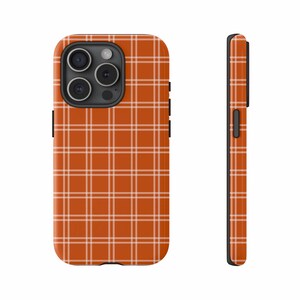 May include: A phone case with a burnt orange plaid pattern. The case has a black camera module and black side buttons. The plaid design features thin white lines creating a grid pattern across the surface.